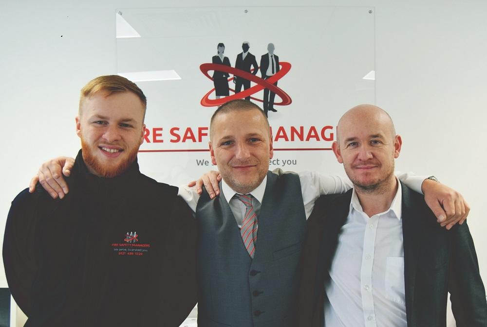 3 men smiling with their arms around each other with the Fire Safety Managers logo in the background