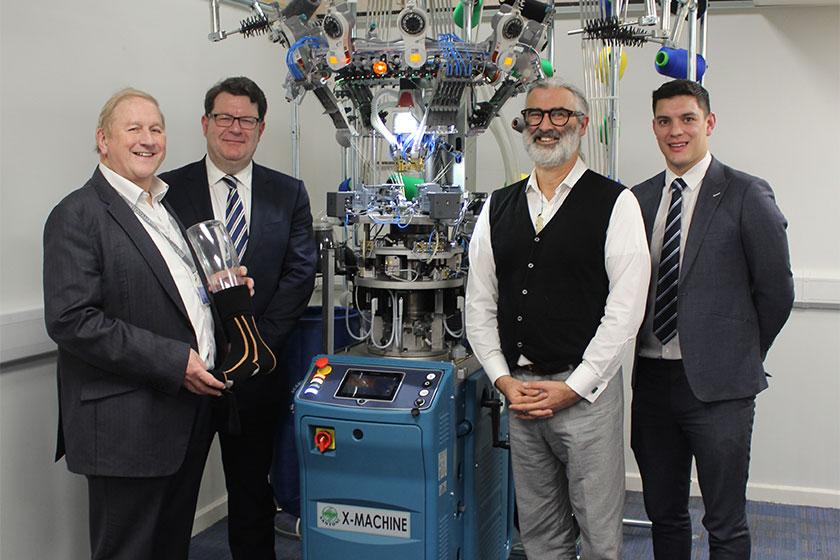 4 men stood next to a textile manufacturing machine