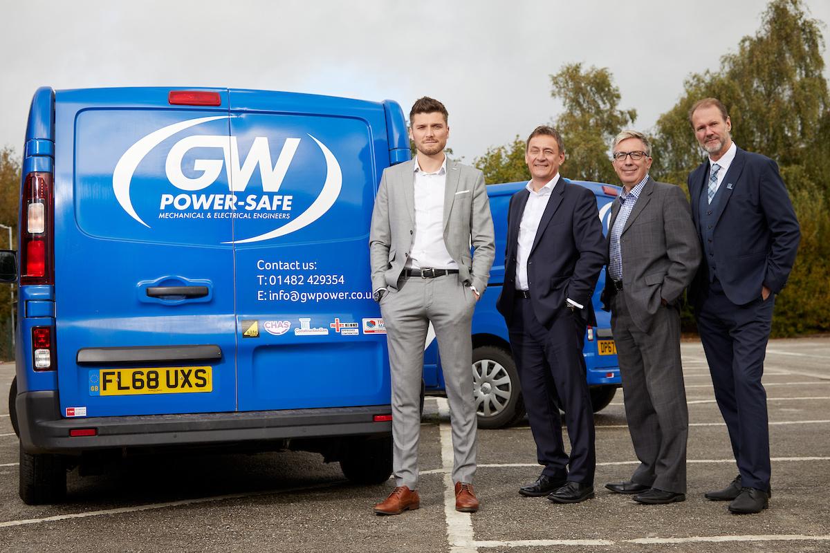 4 men in suits stood in a car park next to GW Power Safe vans