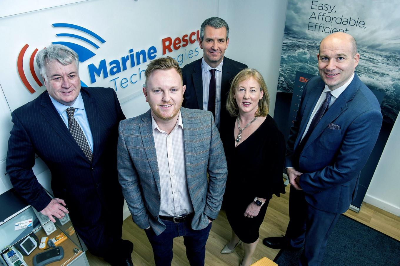 4 men and a woman stood in an office with Marine Rescue Technologies sign in the background