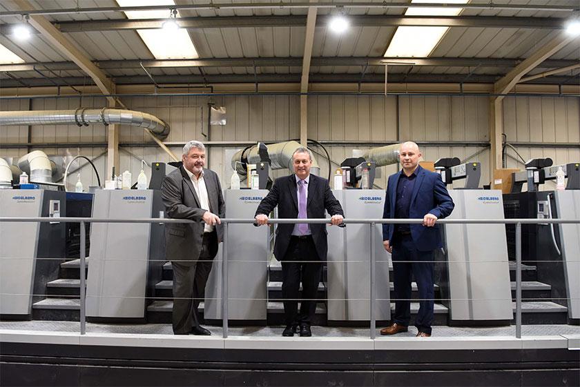 Three men in suits from Streamline Press stood in front of commercial printers