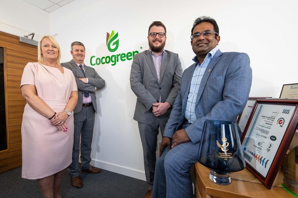 3 men and a woman in a Cocogreen office gathered around an some awards on a table
