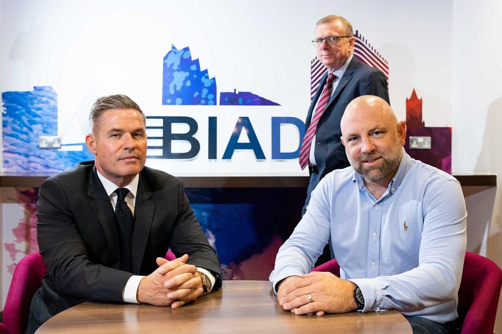2 men sat at a table with another man and BIAD logo in the background