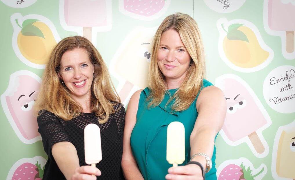2 women from Claudi and Fin holding an ice cream stood in front of a ice cream design wallpaper