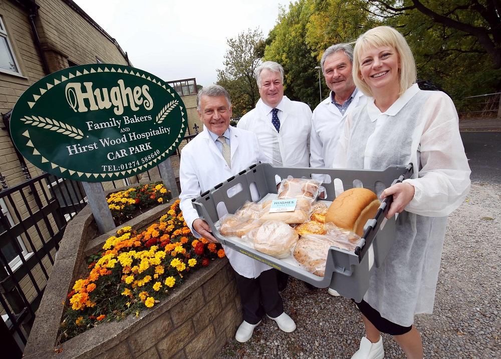 3 men and a woman stood outside of Hughes Bakers holding a basket of fresh bread