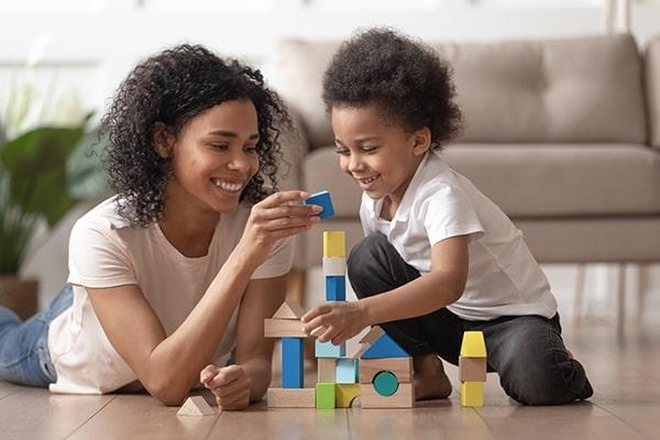 A female nanny and a young boy stacking blocks to make a tower