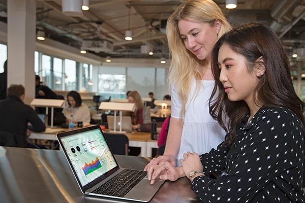 Two young women looking at a laptop displaying Machinelabs software interface