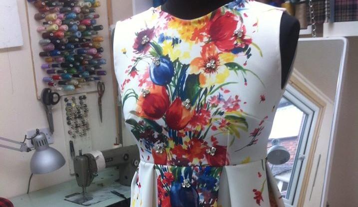 A close up of a floral dress on a mannequin with a sewing machine and threads in the background