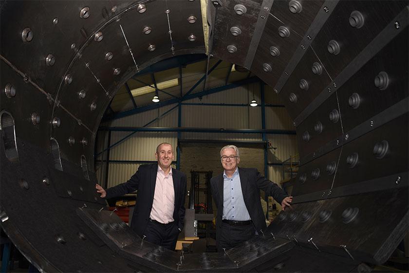 wo men in suits standing behind a vacuum furnace