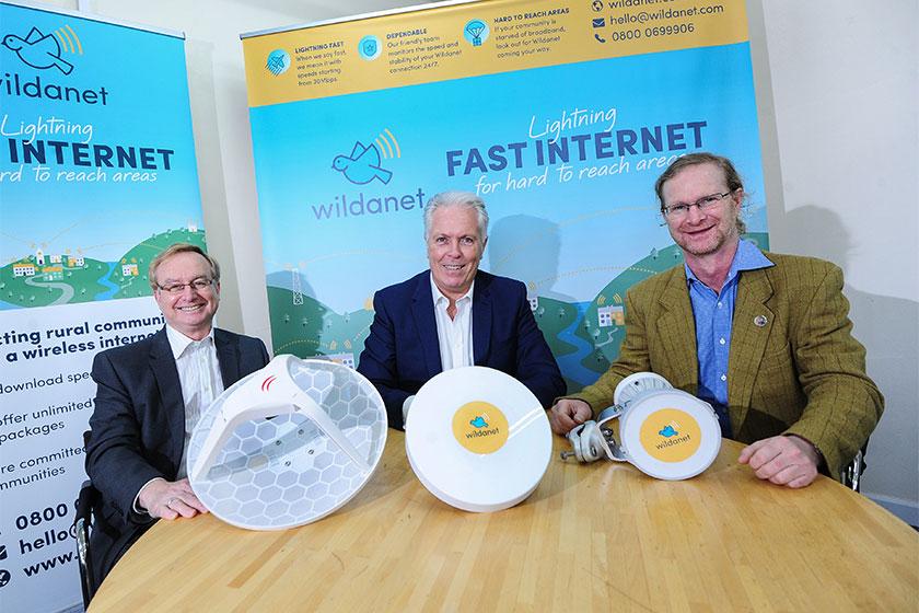 Three men sat at a table showing their broadband product called Wildanet