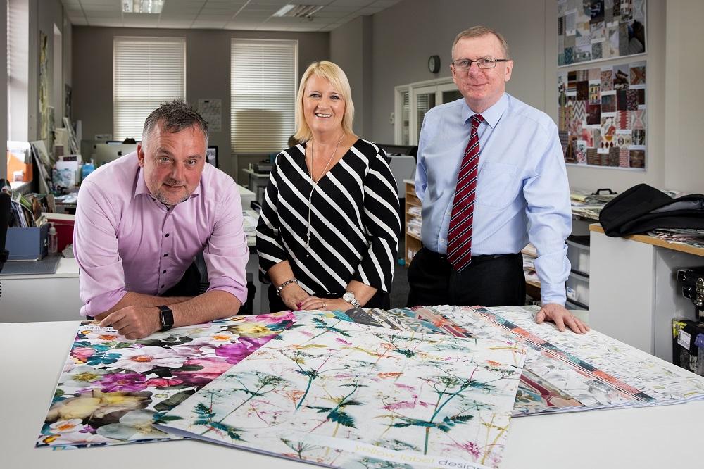 Colleagues from Yellow Label Designs standing in their office and presenting their printed fabrics
