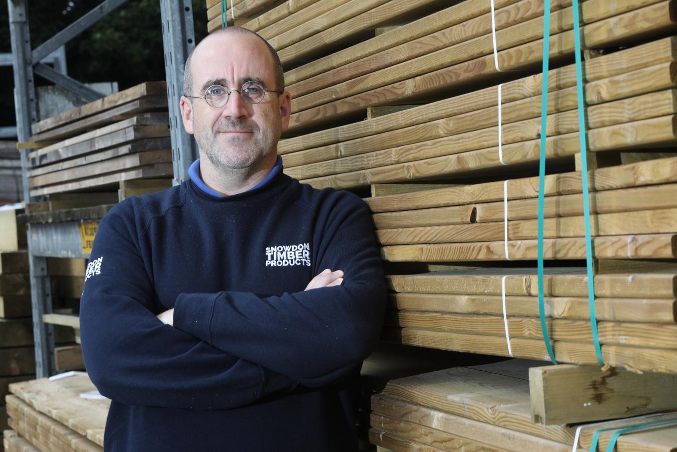 Photo of Jody Goode, Director of Snowdon Timber standing in front of a stock of timber in a warehouse