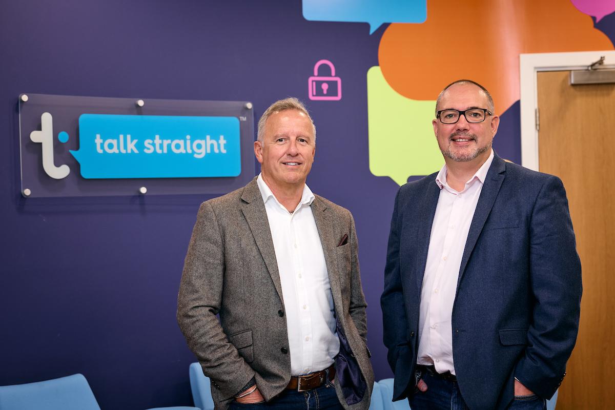 Two men standing in front of talk straight logo